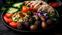 Mediterranean platter with grilled meatballs, hummus, pita bread, fresh vegetables, olives and herbs served on dark plate. Traditional Middle Eastern appetizer.