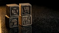 Wooden blocks with carved business icons including shopping cart, umbrella, and stairs symbols on dark textured surface for corporate branding concepts.