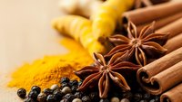 Aromatic spices collection with cinnamon sticks, star anise, turmeric powder, ginger root and black peppercorns arranged on wooden surface for cooking.