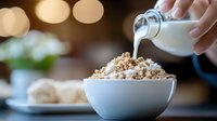 Pouring fresh milk into bowl of crunchy breakfast cereal with blurred warm background creates cozy morning atmosphere. Perfect for food and lifestyle content.