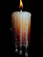 Burning candle with melting wax forming dramatic icicle-like drips against dark background, illuminated by warm flame light creating atmospheric mood.