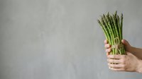Fresh green asparagus bunch held in hands against neutral background, suitable for healthy eating, cooking, nutrition, and food photography projects.