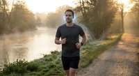 Young athletic Caucasian man jogging on rural path during golden hour sunrise with peaceful river and trees in background for fitness and wellness concepts.