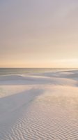 Serene beach landscape with rippled sand dunes and gentle waves under soft pastel sunset sky creating peaceful coastal atmosphere for relaxation content.