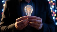 Businessman holding glowing light bulb in hands against blurred city lights background representing innovation, creativity and bright ideas for business success.