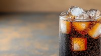 Refreshing cola drink with ice cubes in tall glass showing condensation droplets on dark background. Close up view with selective focus and copy space.