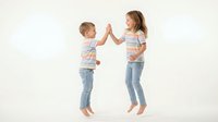 Two happy children giving high five in striped shirts and jeans on white background. Brother and sister celebrating success together in casual clothing.