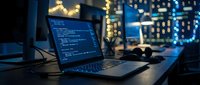 Software developer workspace with laptop displaying code on screen in modern office environment with bokeh city lights background at night.
