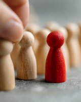 Red wooden pawn figure standing out among natural wooden pawns, symbolizing leadership, uniqueness, and differentiation in business concepts.