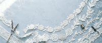 White lace trim and ribbons with floral patterns arranged on soft blue fabric background for wedding, crafts and sewing projects.