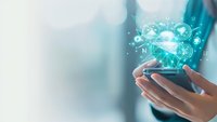 Female hands holding smartphone with glowing network connections and icons floating above screen, soft teal background creates futuristic technology concept.