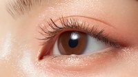 Close-up macro shot of brown eye with long natural eyelashes and clean skin showing detailed iris texture and reflection in bright lighting on peach-toned complexion.