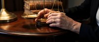 Professional lawyer or judge hands working at wooden desk with golden scales of justice in law office representing legal consultation and judicial decisions.