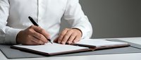 Professional businessman in white shirt writing with pen on documents at modern office desk for business planning and contract signing.