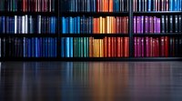 Colorful book spines arranged in rainbow order on dark wooden library shelves create dramatic lighting effect with reflection on glossy surface. Perfect for education themes.