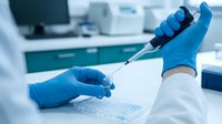 Scientist in blue latex gloves holding pipette over sample plate in modern laboratory setting. Suitable for medical research, biotechnology, and healthcare industry applications.