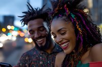 Young African American couple sharing joyful moment outdoors at night. Woman with colorful braids and man with dreadlocks laughing together against blurred city lights.