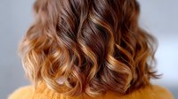 Wavy brown hair with golden caramel balayage highlights shown from behind, demonstrating modern hair coloring technique and styling for salon and beauty industry.