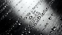 Water droplets on brushed metal surface creating abstract pattern with selective focus and dramatic lighting effects for modern industrial design backgrounds.