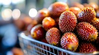 Fresh ripe pulasan fruits with red spiky skin in market basket, selective focus on tropical exotic produce against blurred background with bokeh lights.