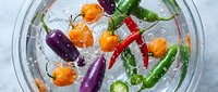 Colorful assorted hot chili peppers submerged in sparkling water in a glass bowl, top view, fresh vegetables with bubbles on light background.