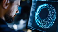 Caucasian male programmer analyzing glowing digital sphere visualization on computer screen in dark office environment with blue technology interface.