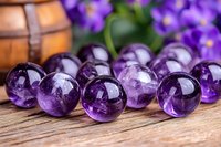 Polished amethyst crystal spheres arranged on rustic wooden surface with purple flowers in background, showcasing natural mineral beauty and spiritual wellness.