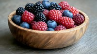 Fresh mixed berries including raspberries, blackberries and blueberries in wooden bowl on gray stone background. Natural healthy food photography.