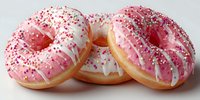 Three glazed donuts with pink and white icing topped with colorful sprinkles on white background, isolated bakery pastries ready for design use.