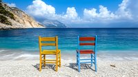 Two colorful wooden chairs on pristine beach with turquoise water and dramatic cliffs. Summer vacation concept for travel and relaxation destinations.