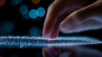 Finger touching glowing sparkles on reflective surface with blue bokeh background creates magical atmosphere. Macro photography captures ethereal light and motion.