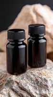 Dark amber glass bottles with black ribbed caps on natural stone surface, soft neutral background creates minimalist composition for wellness and aromatherapy products.