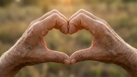 Elderly hands forming heart shape gesture outdoors, expressing love and care in golden sunlight with warm bokeh background for wellness concepts.