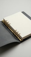 Open leather notebook with blank pages and gold spiral binding on neutral background for business planning and note-taking.