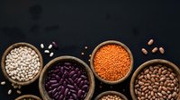 Assorted legumes and beans in wooden bowls on dark background including lentils, chickpeas and kidney beans for healthy cooking and nutrition.