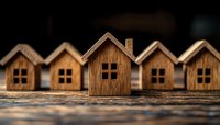 Miniature wooden houses arranged in row on rustic surface with selective focus on center house, symbolizing real estate, neighborhood community and housing market.