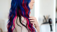 Woman with long wavy hair featuring vibrant blue, pink, and black color blocking. Side profile view showcasing multi-tonal hair coloring technique. Suitable for beauty, fashion, and hair salon marketing.