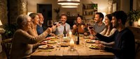 Multigenerational family gathered around wooden dining table sharing meal, wine and conversation in warm lit home interior with candlelight ambiance.