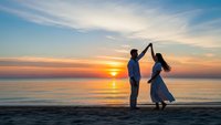Romantic couple dancing on beach at sunset with golden sky and ocean waves, silhouette of man and woman in love enjoying peaceful evening together by sea.