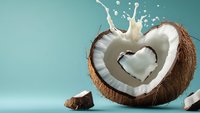 Fresh coconut half with heart-shaped milk splash against turquoise background, dynamic food photography showing white tropical fruit flesh and liquid motion.