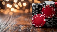 Stacked poker chips in red and black on rustic wooden table with warm glowing bokeh lights creating atmospheric casino gaming background.
