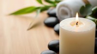 Zen spa composition with burning candle, black stones and bamboo leaves on wooden surface for relaxation and wellness treatments.
