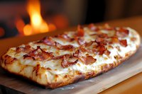 Freshly baked flatbread topped with crispy bacon pieces and melted mozzarella cheese, served on wooden board with warm fireplace in background, creating cozy atmosphere.