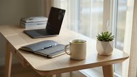 Minimalist workspace with open laptop, notebook, steaming mug, and succulent plant on wooden desk by bright window, ideal for business and productivity content.