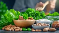 Fresh organic almonds in wooden bowl with green lettuce leaves and broccoli, healthy eating concept with raw nuts and vegetables on rustic table.