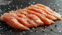 Fresh raw salmon slices with sea salt and peppercorns on dark stone background, arranged in row formation for sushi preparation or cooking.