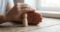 Protective hands cupped over wooden figure symbolizing care, security and support in business insurance concept on rustic table.