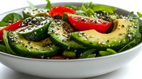 Fresh green salad with sliced avocado, cherry tomatoes, and black chia seeds on white ceramic bowl. Healthy vegetarian meal with arugula leaves and herbs.