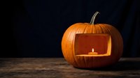 Carved orange pumpkin jack-o-lantern with glowing candle light inside on wooden surface against dark background for Halloween decoration and autumn celebration.