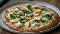 Fresh potato and spinach pizza with melted mozzarella cheese on crispy homemade crust, garnished with aromatic herbs, served on white ceramic plate.